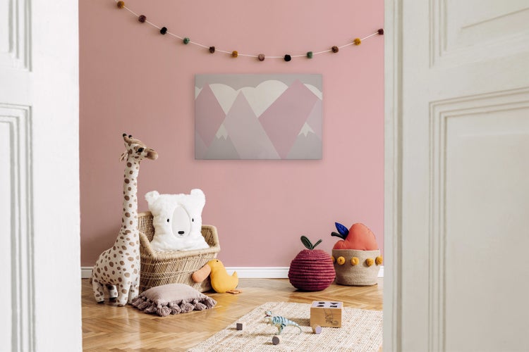 Kinderzimmer mit rosa Wand, Wandbild mit Berggrafik, Giraffenfigur, Rattan-Kindersessel, Stofftieren und Spielzeug auf Holzboden.