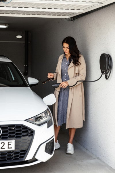 Frau lädt ein Elektroauto in einer Garage mit einer an der Wand montierten Ladestation auf