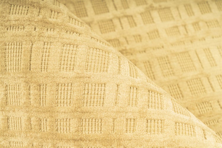 Nahaufnahme eines beigefarbenen gewebten Teppichs mit geometrischem Karomuster und strukturierter Oberfläche.