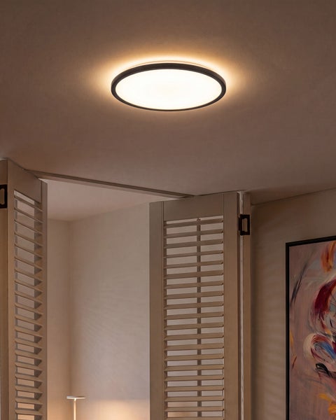 Runde LED Deckenleuchte mit flachem Design, montiert an einer Zimmerdecke in einem Wohnraum mit Lamellentüren.