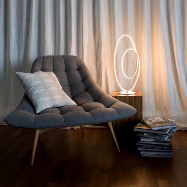 Grauer Sessel mit Kissen, LED-Lampe und Bücherstapel vor Vorhang