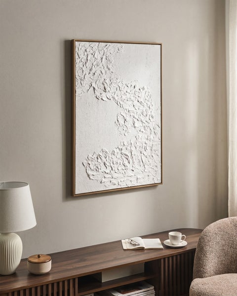 Strukturiertes Wandbild in Weiß mit schmalem Holzrahmen in einem hellen, minimalistischen Wohnzimmer über einem Sideboard.