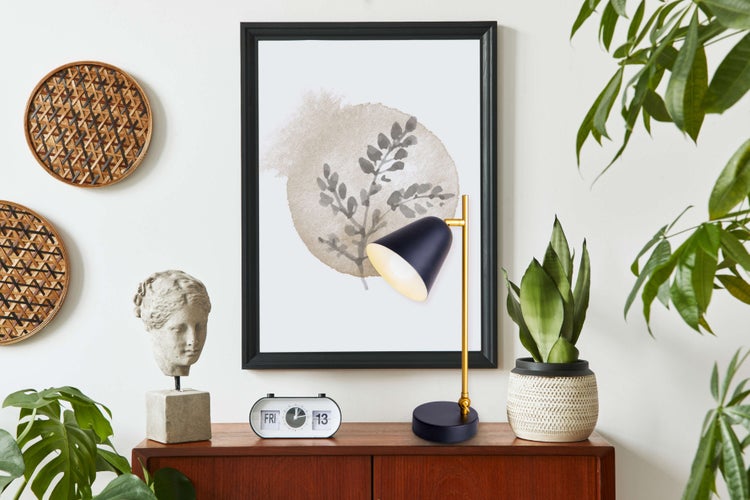 Dekorative Szene mit Bild, Lampe, Uhr, Kopfskulptur und Pflanzen auf einem Schrank