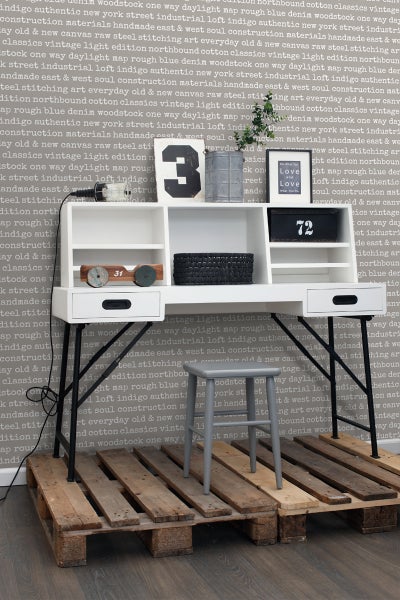 Einrichten mit weißem Schreibtisch mit Schubladen, Ablageflächen und schwarzem Metallgestell, dazu ein grauer Hocker auf einer Holzpalette.