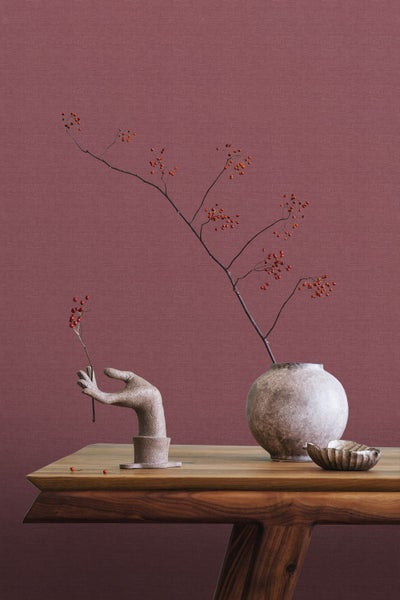 Dekoratives Stillleben mit Vase, Handskulptur und Beerenzweigen auf einem Holztisch vor einer Wand