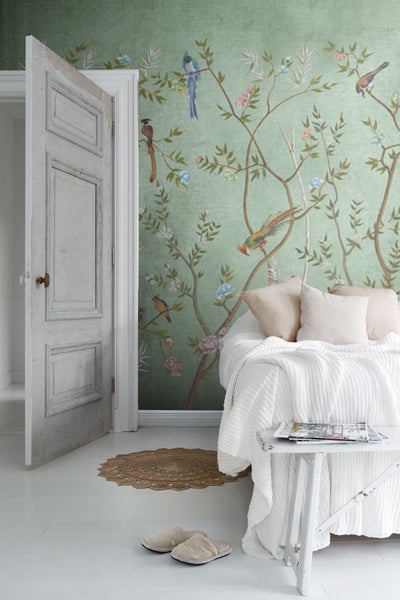 Schlafzimmer mit grün gemusterter Tapete, Bett, kleinem Tisch und geöffneter Tür