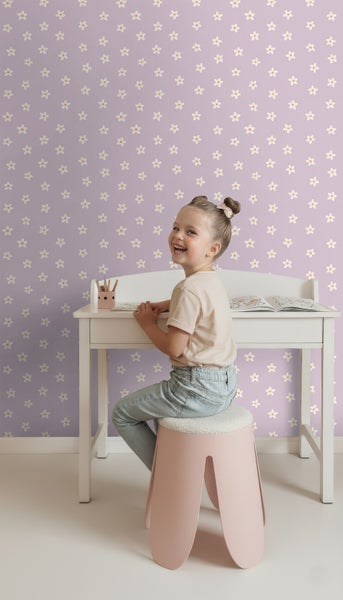 Mädchen sitzt an Schreibtisch vor Tapete mit Blumenmuster