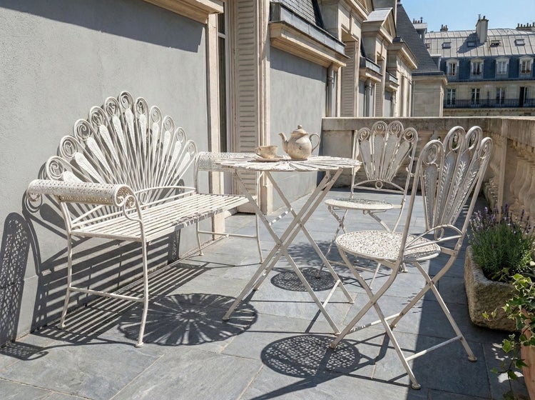 Terrassenszene mit Metallgartenmöbeln, bestehend aus Tisch, Stühlen und Bank, mit Teekanne und Tasse auf dem Tisch
