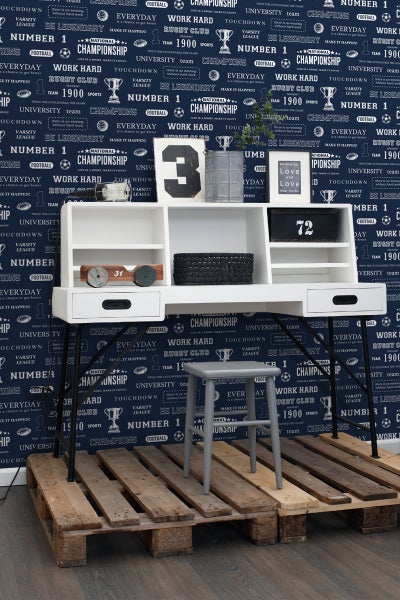 Dekoratives Zimmer mit weißem Schreibtisch und grauem Hocker vor einer Wand mit Motivtapete.