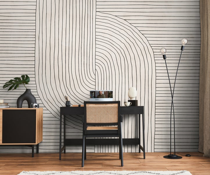 Fototapete mit abstraktem schwarzen Linienmuster in einem modern eingerichteten Arbeitszimmer mit schwarzem Schreibtisch und Rattan-Stuhl.