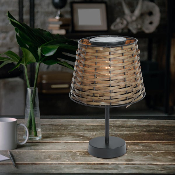 Dekorative Tischleuchte mit Rattan-Schirm auf einem Holztisch