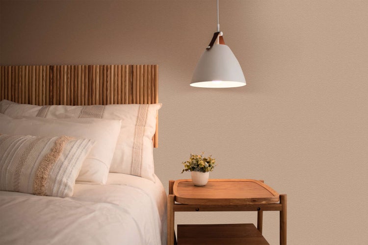 Moderne Pendelleuchte mit Metallschirm und Lederriemen über einem Holznachttisch in einem Schlafzimmer mit Kopfteil aus Holzlamellen.