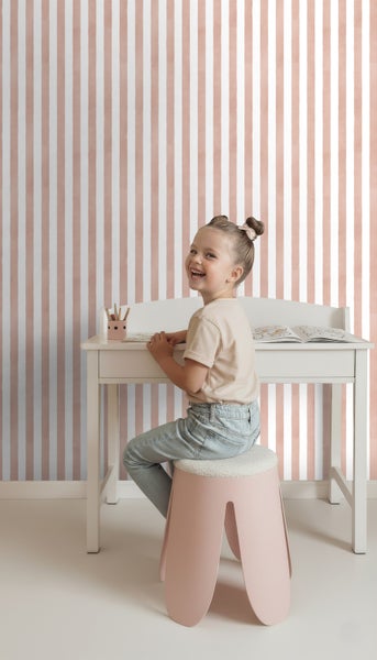 Kind sitzt an einem Schreibtisch vor einer gestreiften Tapete