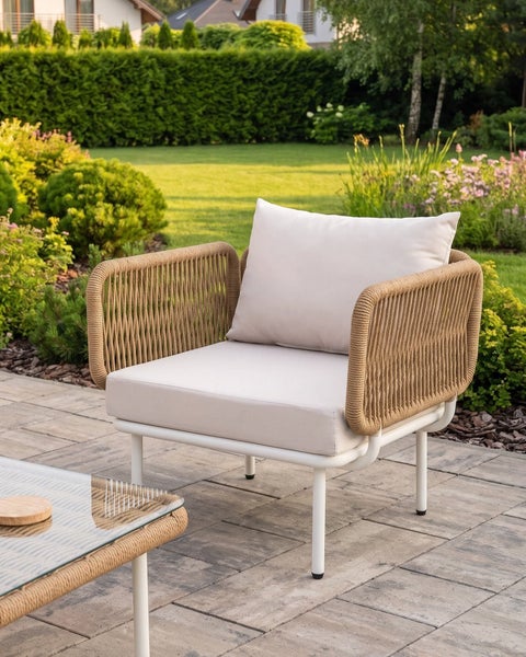 Moderner Outdoor-Sessel mit Seilgeflecht an den Armlehnen, Metallgestell und Polsterkissen auf einer Terrasse im Garten.