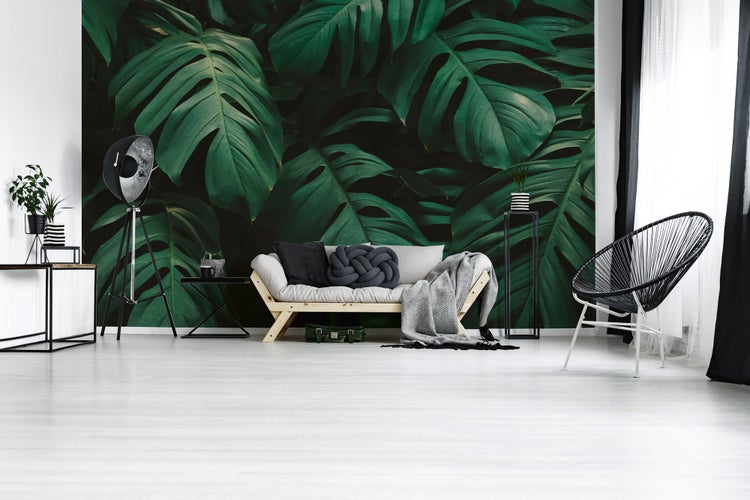 Modernes Wohnzimmer mit Fototapete mit Monstera-Blättern, Holzsofa, Dreibeinlampe und Acapulco-Stuhl.