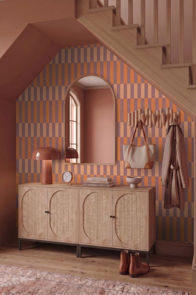 Moderner Flur unter einer Holztreppe mit geometrischer Tapete, hellem Sideboard mit Rattan-Einsätzen und einem Rundbogenspiegel.