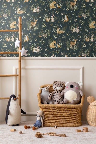 Kinderzimmer mit Vliestapete mit Waldtiermotiven, Bambusleiter, Rattankorb und verschiedenen Kuscheltieren auf einem Teppich.