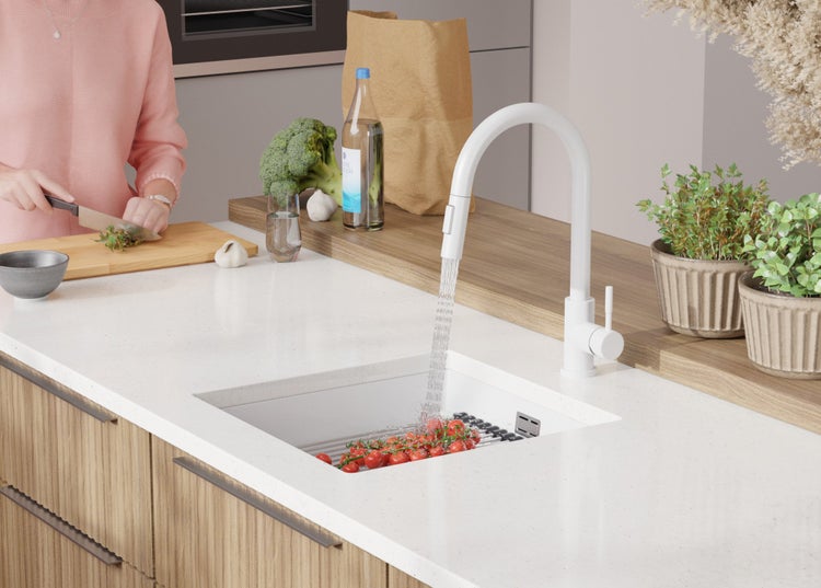 Küchenszene mit Spüle, Armatur, Gemüse und Person beim Kochen.