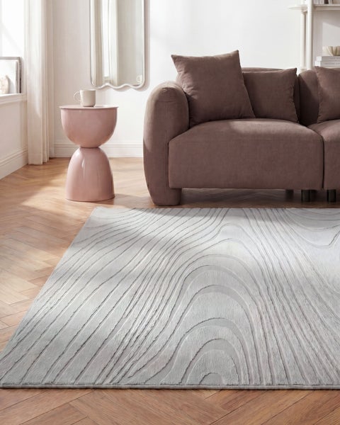 Modernes, helles Wohnzimmer mit strukturiertem Teppich mit Wellenmuster auf Holzparkett neben einem braunen Sofa und einem rosa Beistelltisch.