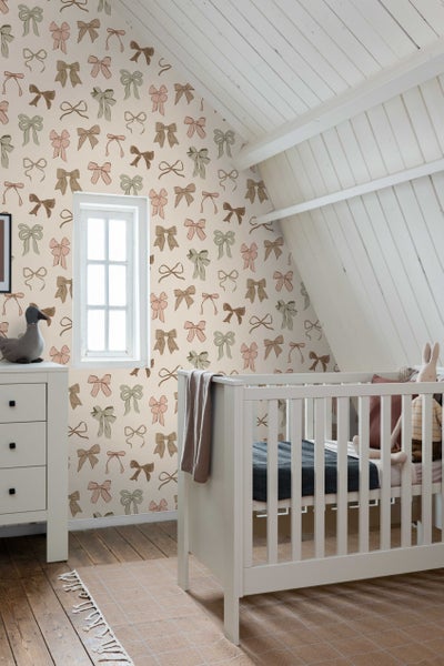 Helles Kinderzimmer mit Kinderbett, Kommode und Tapete mit Schleifenmuster.