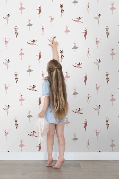 Mädchen berührt Tapete mit Ballerina-Muster in einem hellen Raum.