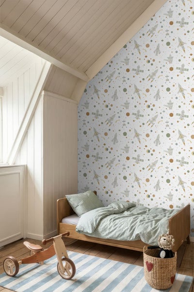 Hell gestaltetes Kinderzimmer mit Weltraum-Vliestapete, Raketen-Motiven, Holz-Kinderbett und hölzernem Dreirad in einer Dachwohnung.