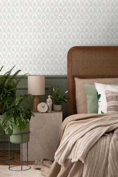 Schlafzimmer mit gemusterter Tapete, Bett und Beistelltisch mit Dekorationen