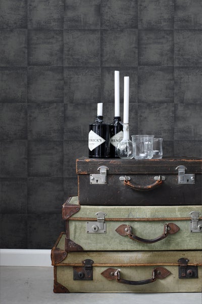 Szene mit gemusterter Tapete, gestapelten Koffern, Getränkeflaschen und Kerzen