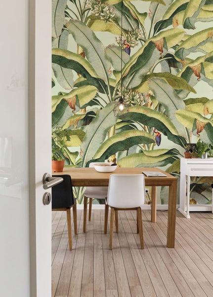 Esszimmer mit Esstisch, Stühlen und Wandtapete mit Bananenblattmuster.