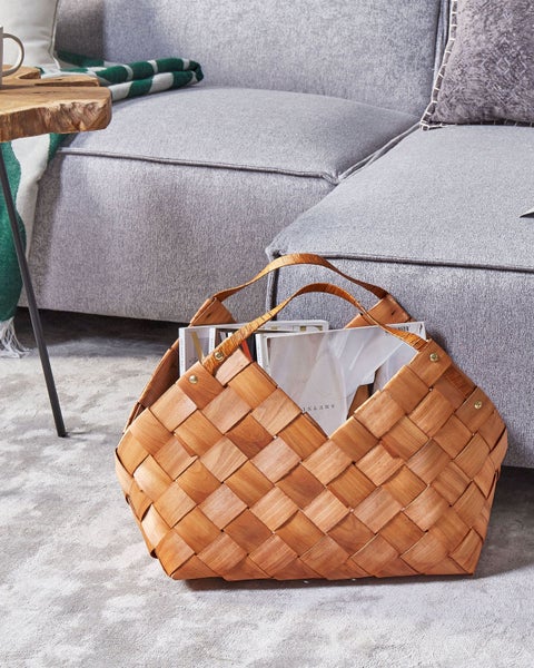 Geflochtener Holzkorb mit Magazinen neben einem grauen Sofa