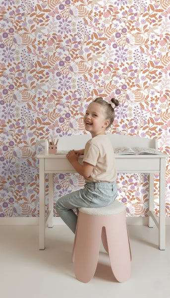 Mädchen sitzt an einem Schreibtisch vor einer floralen Tapete