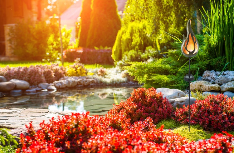 Dekorative Gartenleuchte in Flammenform zwischen Büschen und Gräsern