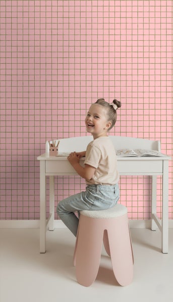 Kind sitzt an einem weißen Schreibtisch vor einer Wand mit quadratischer Tapete.