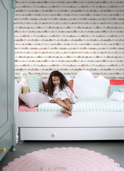 Kinderzimmer mit Mädchen auf Bett, gemusterten Kissen und runder Teppich