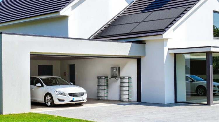 Modernes weißes Haus mit Photovoltaikanlage auf dem Dach, Garage mit Auto und installiertem Heimspeichersystem an der Wand.