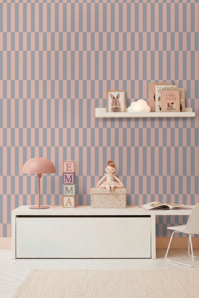 Kinderzimmer mit geometrisch gemusterter Tapete in Rosa und Grau, weißem Sideboard und Wandregal mit Dekoration.