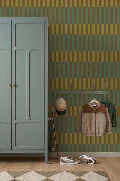 Kinderzimmer mit gestreifter Tapete in Grün und Ocker, einem salbeigrünen Schrank, Garderobe mit Jacke, Skateboard und Schuhen auf Holzboden.
