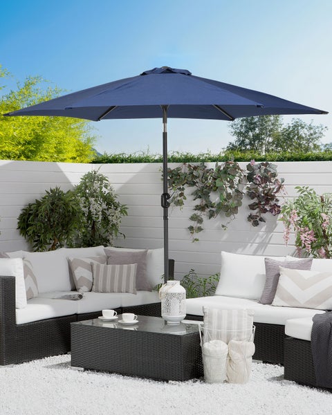 Großer blauer Sonnenschirm über einer modernen Lounge-Garnitur aus dunklem Polyrattan mit weißen Kissen auf einer Kiesterrasse.