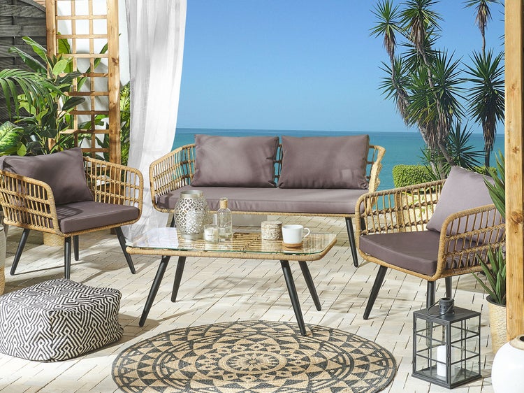 Terrassenszene mit Rattansitzgruppe, bestehend aus Sofa, Sesseln und Tisch mit Glasplatte, ergänzt durch Outdoor-Teppich und Dekoration