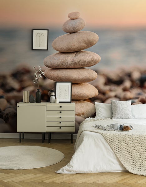 Modernes Schlafzimmer mit Vliestapete einer Steinpyramide am Strand, hellem Sideboard, Parkettboden und einem Bett in ruhiger Atmosphäre.