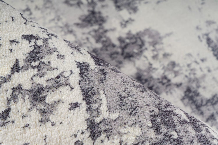 Nahaufnahme eines flauschigen Teppichs mit abstraktem grau-weißem Marmormuster und weicher Oberflächenstruktur.