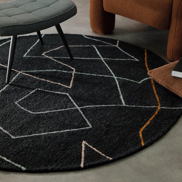 Runder schwarzer Teppich mit geometrischem Linienmuster aus weißen und gelben Linien in einem Wohnzimmer.