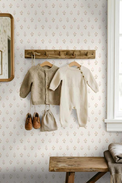 Helles Kinderzimmer mit floral gemusterter Tapete, einer hölzernen Garderobe mit Babykleidung und einer rustikalen Holzbank.