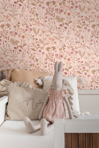 Vliestapete mit filigranem Blumenmuster und Gräsern im Kinderzimmer hinter einem Bett mit Kissen und Stofftier.