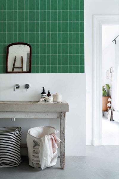 Badezimmer mit Wandfliesen im Hochformat an der Wand, kombiniert mit einem rustikalen Waschtisch aus Beton und einem antiken Wandspiegel.
