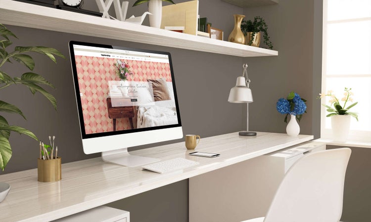 Moderner Arbeitsplatz mit Computer auf hellem Schreibtisch, Monitor zeigt Tapetenmuster, dekorierte Regale an der Wand.