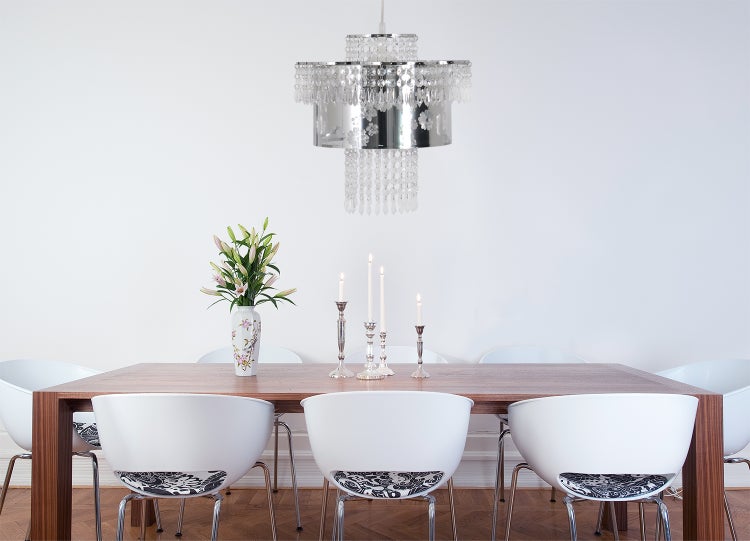 Esszimmer mit Holztisch, weißen Stühlen, Kristalllüster, Blumenvase und Kerzenständern