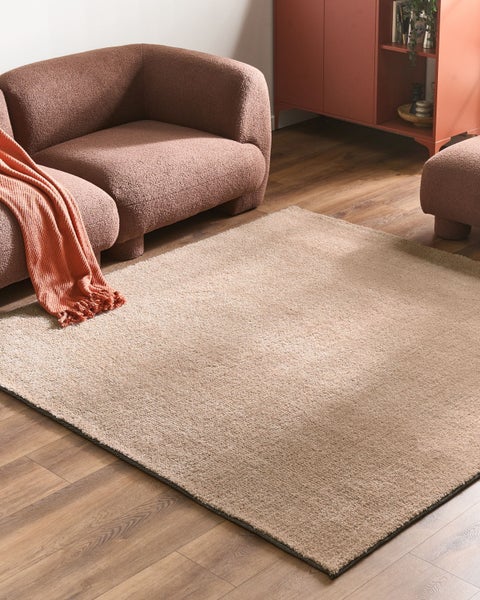Rechteckiger Hochflor-Teppich in einem modernen Wohnzimmer mit strukturiertem Sessel, Hocker und Holzboden.