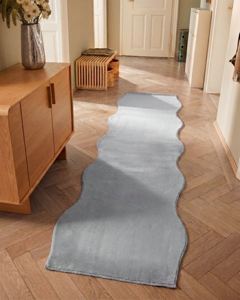 Hellblauer Läufer mit gewelltem Rand auf hellem Parkettboden in einem hellen Flur mit Sideboard und Holzbank.