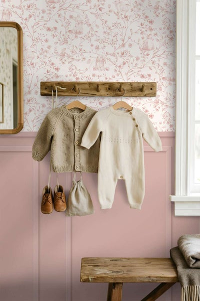 Vlies-Tapete mit Häschen- und Blumenmuster in einem Kinderzimmer mit Holzgarderobe und hängender Babykleidung.